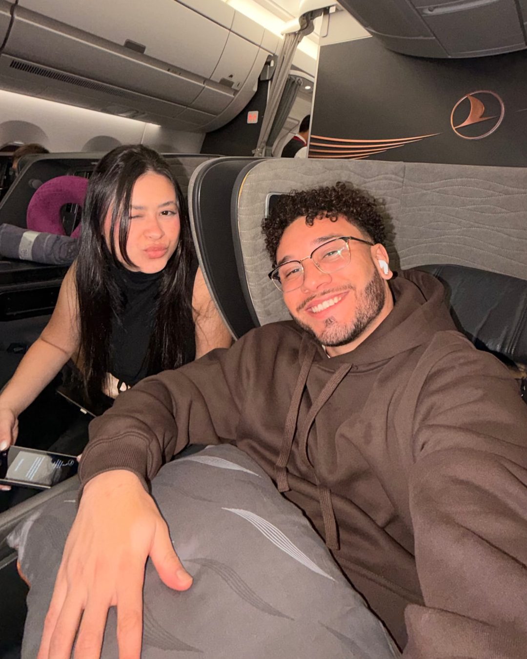 Gustavo e Letícia sorrindo lado a lado nas poltronas da classe executiva da Turkish Airlines