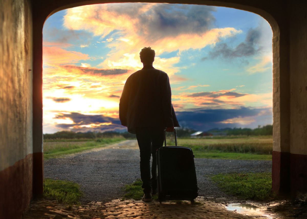 Pessoa com uma mala de viagem saindo de um portal escuro para um campo aberto ao entardecer